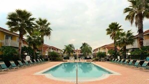 Una piscina con sillas de descanso y palmeras, rodeada de edificios.