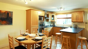 Una cocina moderna con armarios de madera, una zona de comedor con una mesa preparada para dos personas y una isla grande con taburetes.