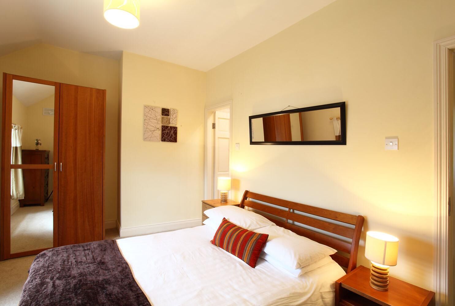 Ein Schlafzimmer mit einem hölzernen Bett, weißer Bettwäsche, einem Spiegel und zwei Nachttischlampen.