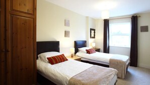 Habitación de hotel con dos camas individuales, un armario de madera, un televisor y una ventana con cortinas.