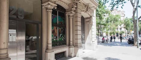 Une façade d’immeuble présentant des éléments d’architecture classique, notamment des colonnes richement décorées et une grande fenêtre en arc surmontée de barreaux métalliques.