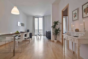 A spacious living area with a dining table, chairs, a potted plant, and a white console table with candles.