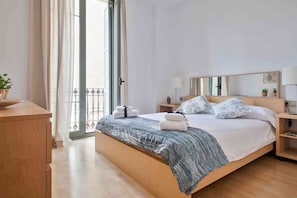 A hotel room with a bed, bedside lamps, a wooden nightstand, a window with curtains, and a view of the outside.
