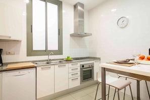 A modern kitchen with white cabinets, a stainless steel range hood, a built-in oven, and a window above the sink.