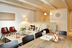En hyggelig stue med et træbord, to brune læderstole, en beige sofa med puder, en lampe og et ur på væggen.