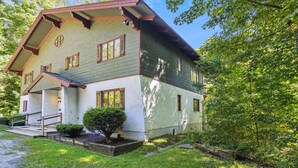 Une maison à deux étages, avec un toit en pente, un porche à l’avant et un petit jardin devant.