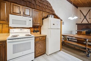 A kitchen with wooden cabinets, a stove, a microwave, a refrigerator, and a dining area with benches. - 4-Bedroom Townhouse with Sauna - Flurry (Killington)