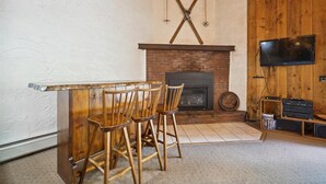 Ein gemütliches Wohnzimmer mit Kamin, Holzstühlen, Fernseher und Bücherregal.