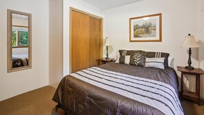 Une chambre à coucher avec un lit, deux tables de chevet, un miroir, une porte en bois et un tableau encadré accroché au mur.