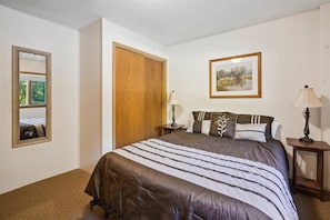 Een slaapkamer met een bed, twee nachtkastjes, een spiegel, een houten deur en een lijst met een afbeelding aan de muur.