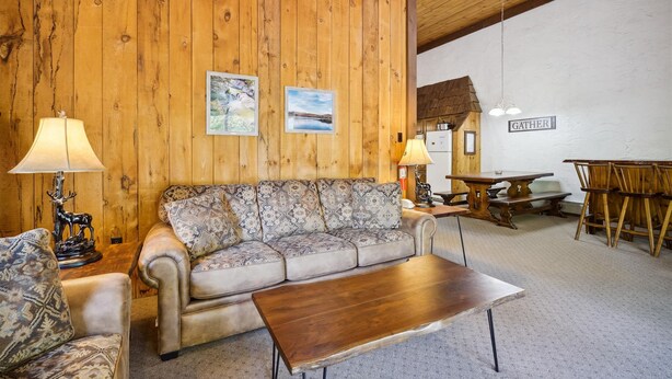 Une pièce chaleureuse avec un mur en bois, un canapé, une table basse et un coin repas comprenant une table et des chaises.