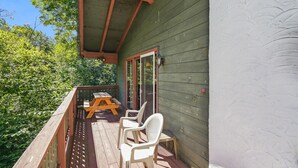 Une terrasse en bois avec une table de pique-nique et des chaises, un espace abrité et une vue sur les arbres.
