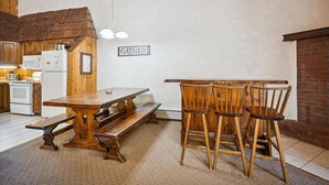 Une cuisine rustique avec des armoires en bois, une table en bois et un banc. Il y a une pancarte sur le mur où est écrit « RASSEMBLEMENT ».