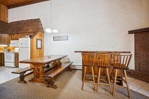 Een rustieke keuken met houten kastjes, een houten tafel en een bank. Op de muur hangt een bord waarop staat 