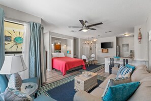 Quarto de hotel moderno com cama, sofá, mesa de centro, televisão e ventoinha no teto.
