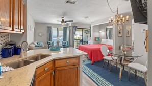 Ein modernes Hotelzimmer mit Küchenbereich, Esstisch, Bett und Blick ins Freie.