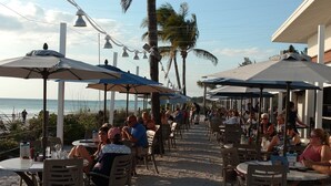 An outdoor dining area with tables and chairs, umbrellas, and palm trees. - Sunset Condo #156 on Anna Maria Island (Bradenton Beach)