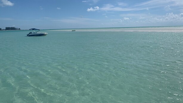 A boat on clear turquoise water with a sandy beach and a distant shoreline. - Sunset Condo #156 on Anna Maria Island (Bradenton Beach)