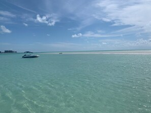 A boat on clear turquoise water with a sandy beach and a distant shoreline.