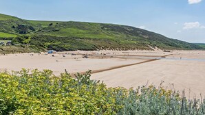 Una spiaggia costiera con tende e un piccolo edificio, circondata da dolci colline verdi.