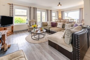 Un salon chaleureux avec un canapé, un fauteuil et une table basse, de grandes fenêtres avec des rideaux et une cheminée.
