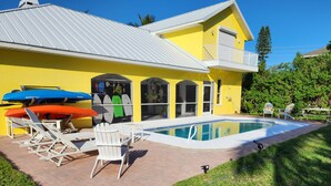 Une maison jaune avec une piscine, des chaises blanches et des planches de surf.