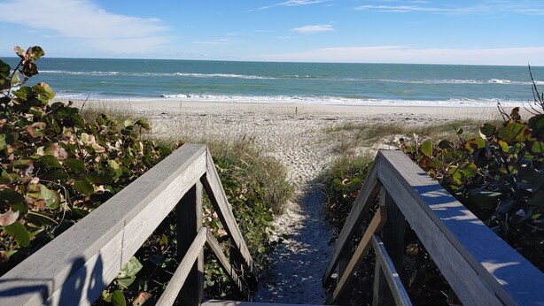 Une promenade en bois qui mène à une plage, avec des vagues en arrière-plan.