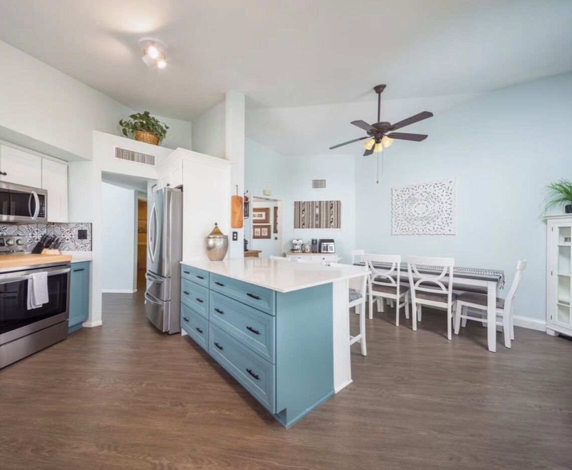 A modern kitchen with a central island, white cabinets, and a dining area with a white table and chairs.