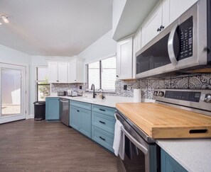 A modern kitchen with white cabinets, a wooden countertop, and a stainless steel microwave. - Tucson Omni Oasis – 4BR-3BA Desert Retreat with Private Hot Tub & Fire Pit (Tucson)