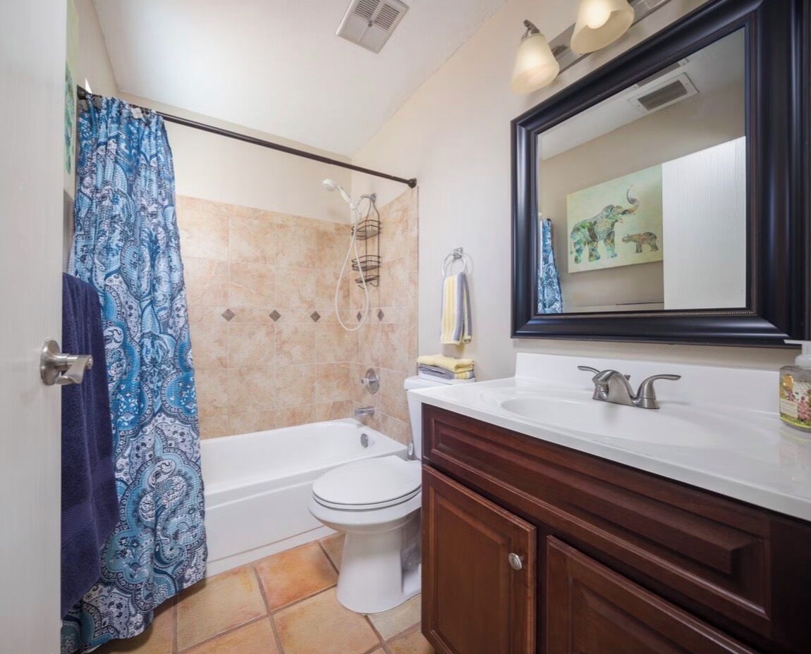 A bathroom with a shower, toilet, sink, and mirror.
