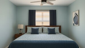 A bedroom with a bed, a nightstand, a lamp, a ceiling fan, and a window with curtains. - Tucson Omni Oasis – 4BR-3BA Desert Retreat with Private Hot Tub & Fire Pit (Tucson)