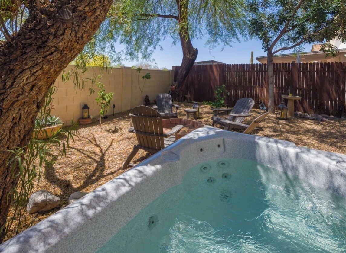 A hot tub surrounded by outdoor furniture, a tree, and a wooden fence.