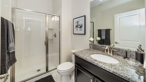 A modern bathroom with a glass-enclosed shower, a white toilet, a granite countertop sink, and a large mirror.