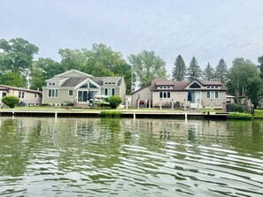 A row of cabins by a calm lake, with docked boats and a grassy deck.
