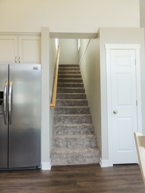 Una cocina con un refrigerador de acero inoxidable, una escalera de madera y una puerta blanca.