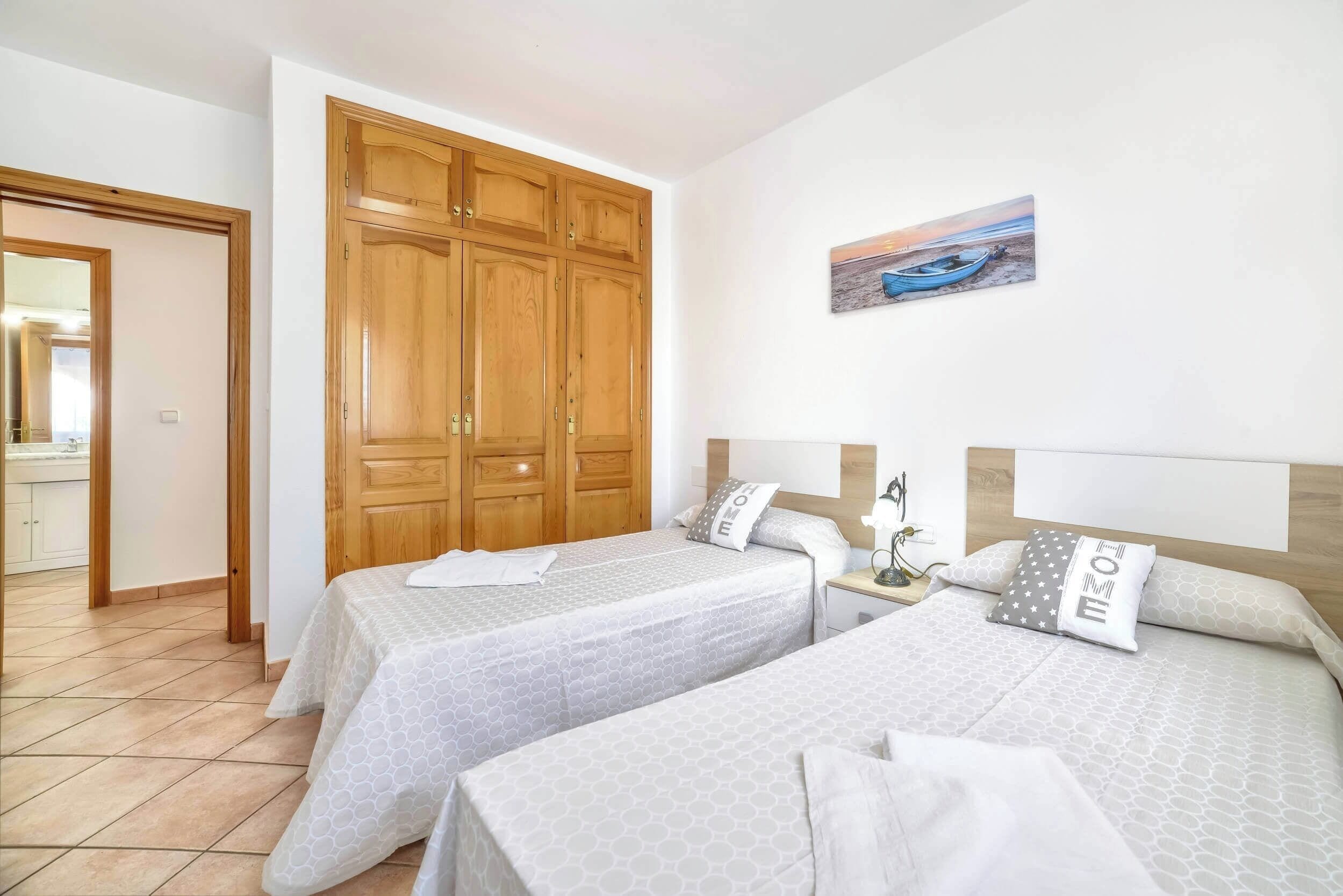 Ein Hotelzimmer mit zwei Betten, einem Holzschrank, einem Bild mit Strandmotiv und einem Fliesenboden.