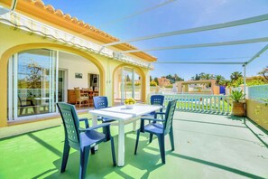 A covered outdoor patio with a table and chairs, a pool in the background, and a view of the surrounding neighborhood.