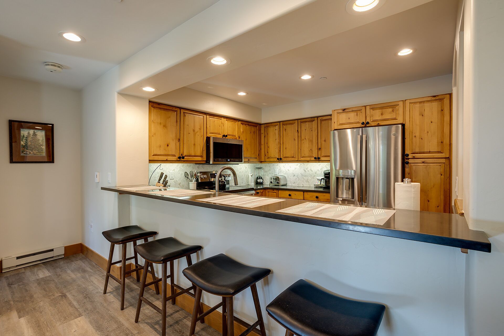 A modern kitchen with wooden cabinets, stainless steel appliances, and a bar area with stools.