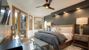 A bedroom with a bed, bedside tables, a bench, a ceiling fan, and large windows.