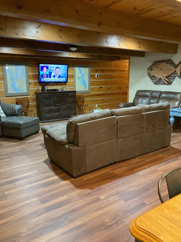 Ein gemütliches Wohnzimmer mit einem braunen Ecksofa, einer Holzboden und einem Fernseher, sowie einer Karte an der Wand.