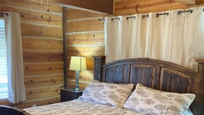 Een slaapkamer in een houten blokhut, met een bed, nachtkastje, lamp en plafondventilator.