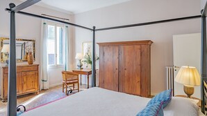 Ein Schlafzimmer mit einem Himmelbett, einem Holzschrank, einem Schreibtisch mit Stuhl und einem fenster mit Vorhängen.
