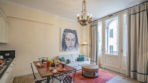 Ein Essbereich mit einem für das Frühstück gedecktem Tisch, einer Couch und einem großen Fenster mit Vorhängen.
