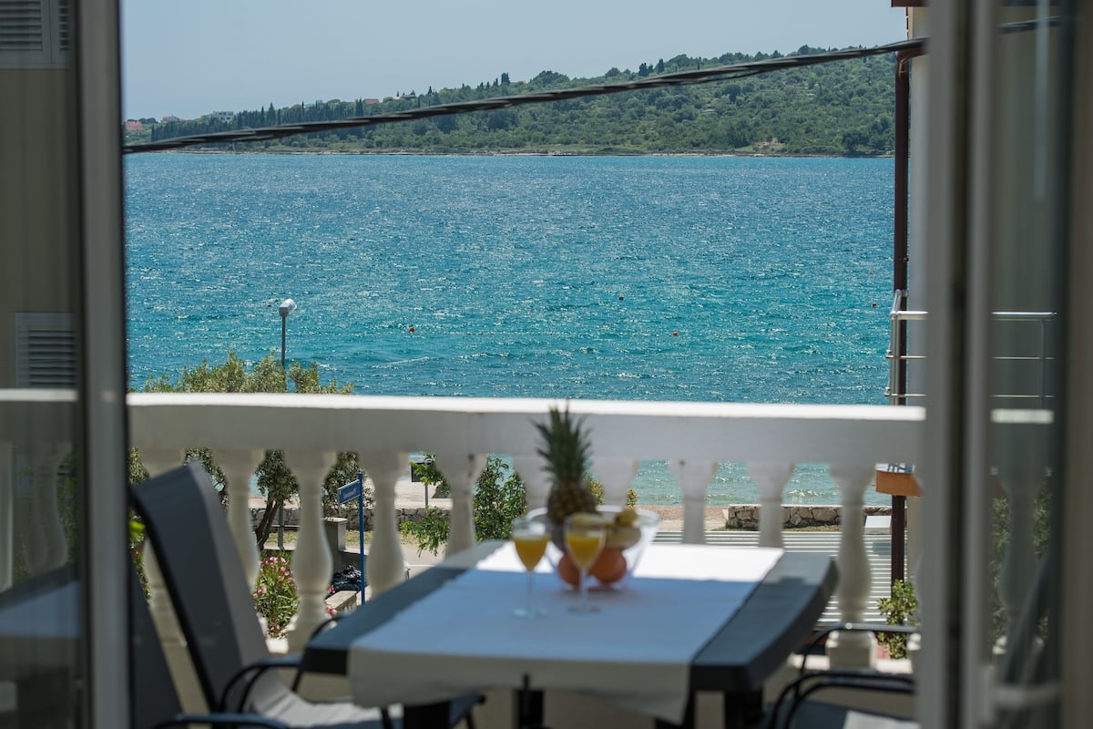 A balcony with a table set for two, overlooking a large body of water and a bridge.