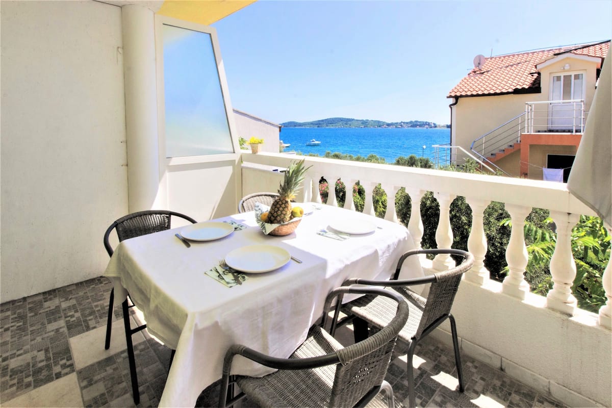 A balcony with a table set for two, overlooking a coastal view.