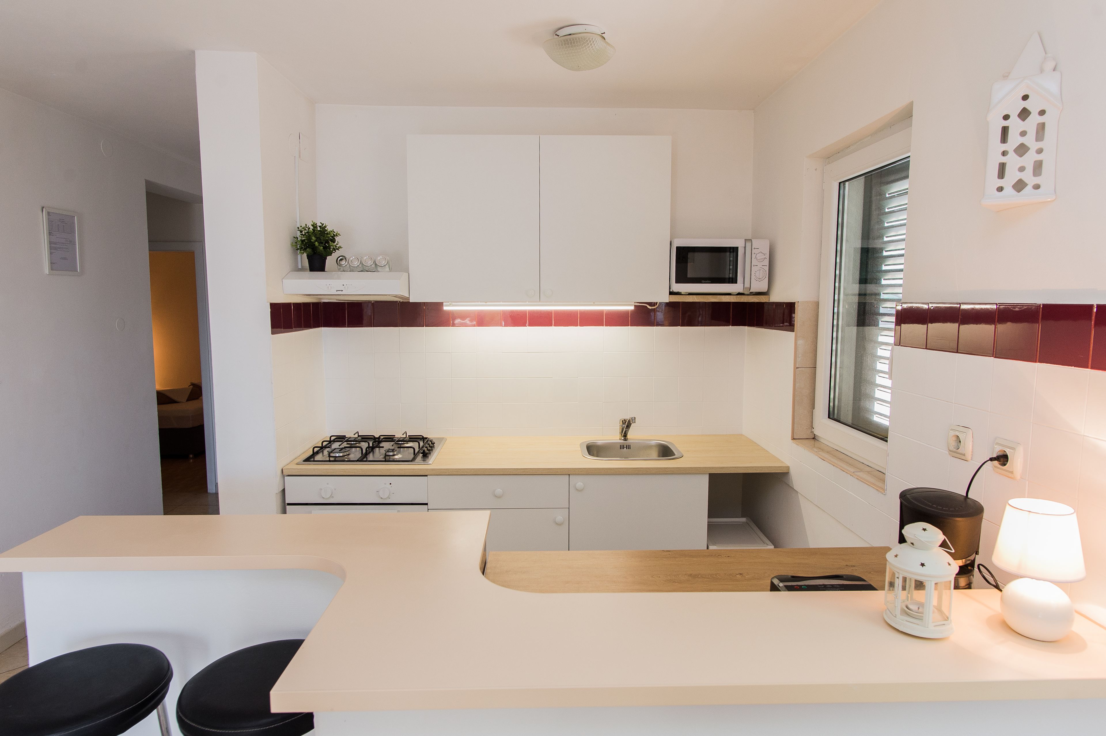 Una cucina moderna con mobili bianchi, un forno a microonde, un piano cottura a gas e un lavello. Due sgabelli neri sono presenti al bancone.