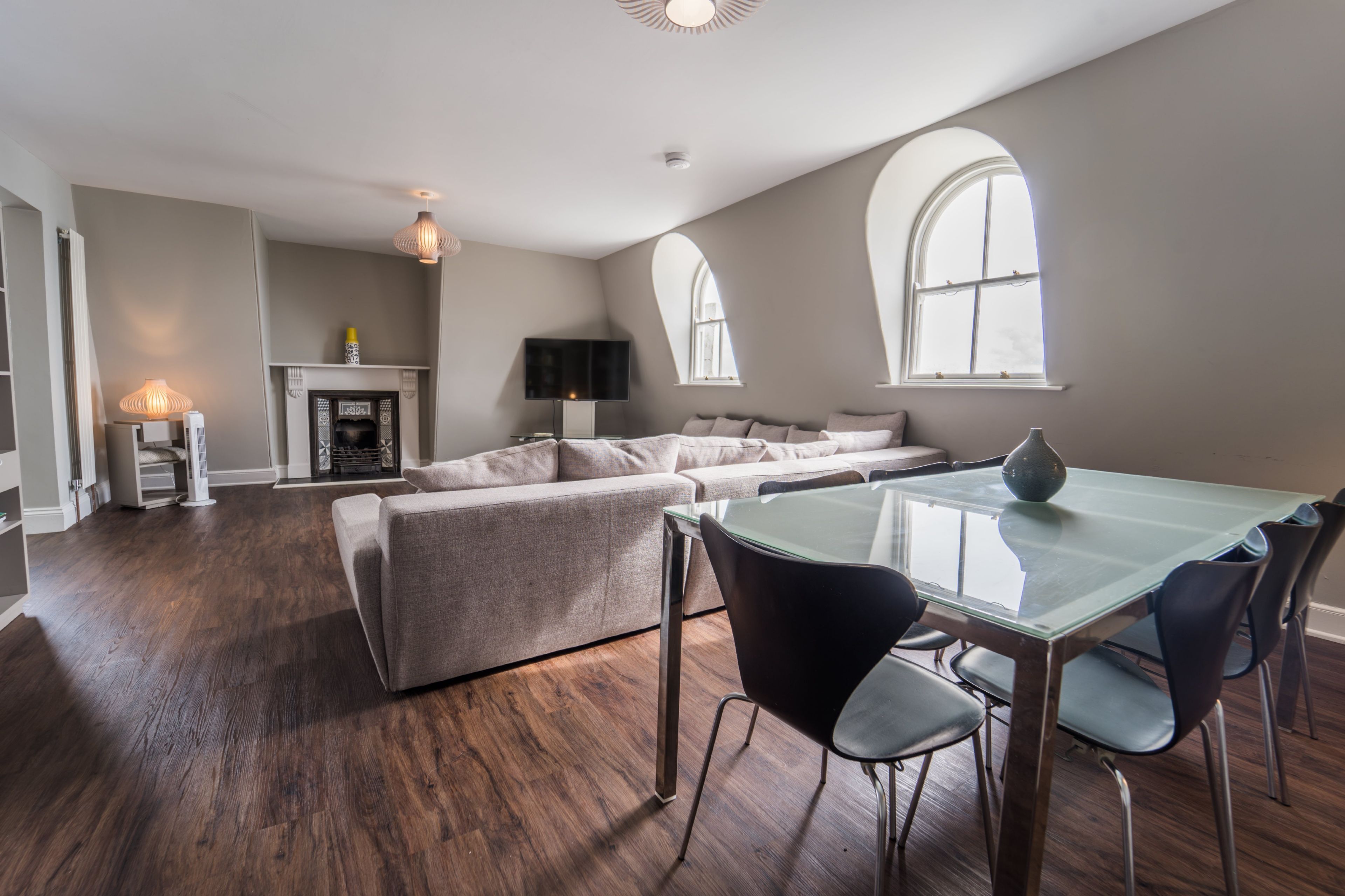 A spacious living area with a sofa, a glass dining table, and a fireplace.