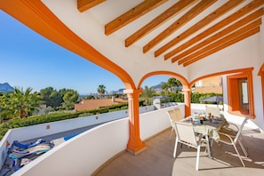 A balcony with a table and chairs, overlooking a scenic view of mountains and a cityscape. - Villa Altamira - Plus (Calpe)