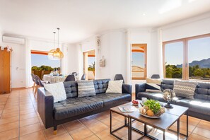 A modern living room with a black leather sofa, a coffee table, and a dining area with a table and chairs. - Villa Altamira - Plus (Calpe)