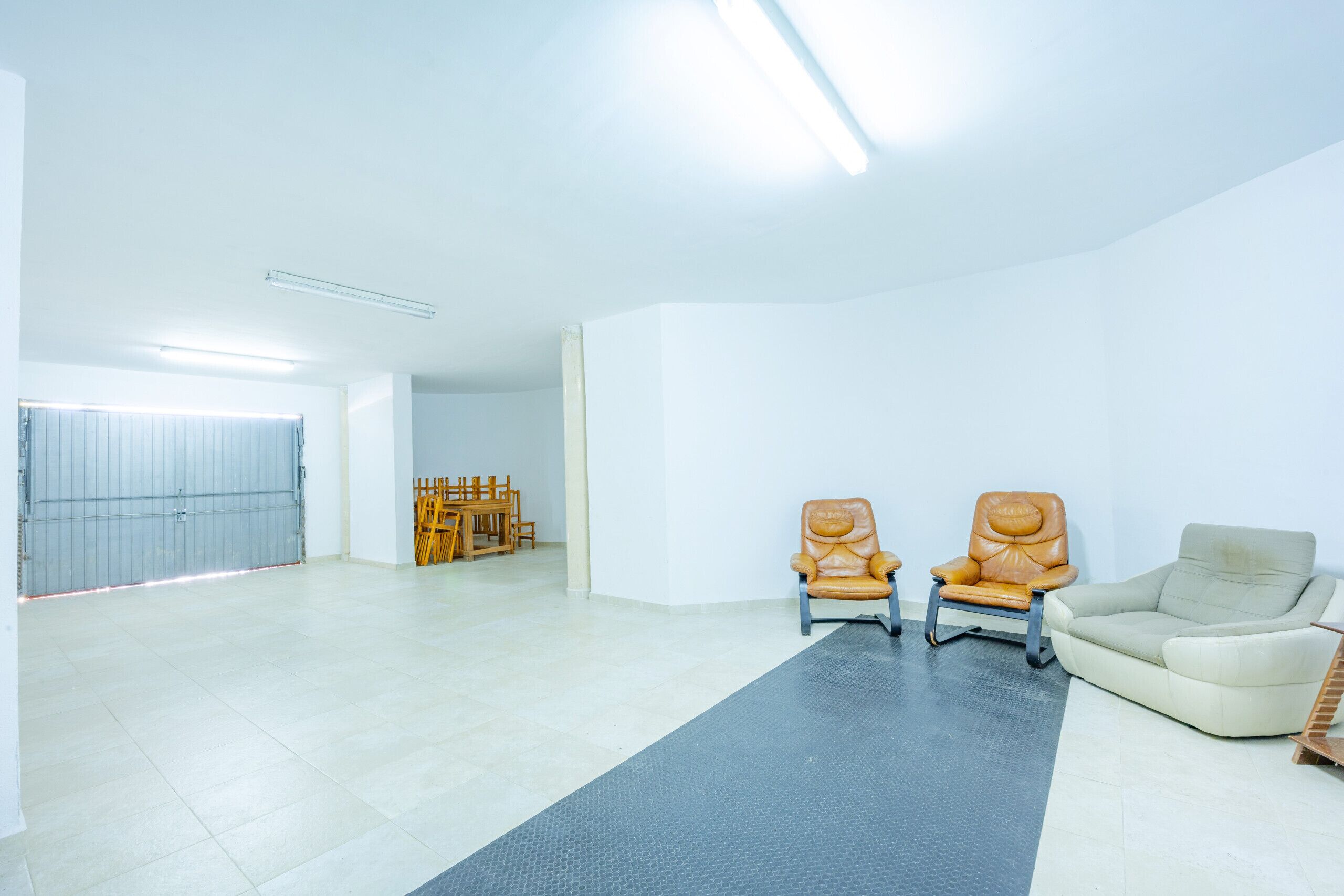 Amplia habitación con una alfombra gris grande, dos sillones de cuero, un sofá color beige y una puerta cerrada.